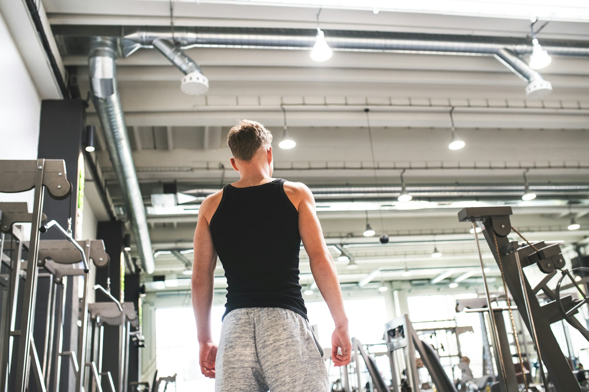 A beginner walking into a gym, looking at people lifting heavy weights, and feeling motivated to start their muscle-building journey.