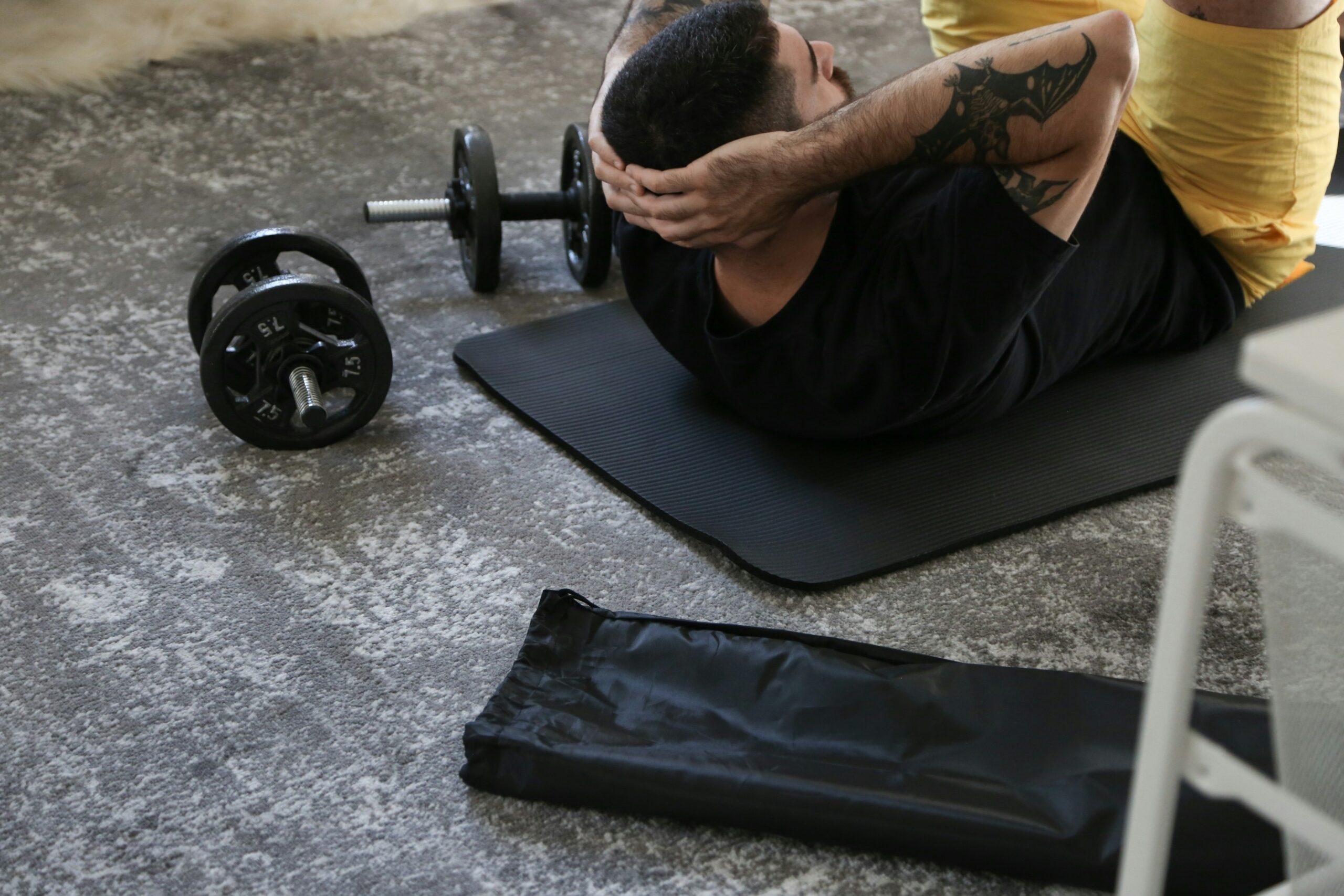 Person exercising at home with a yoga mat and dumbbells, highlighting the convenience and flexibility of home workouts